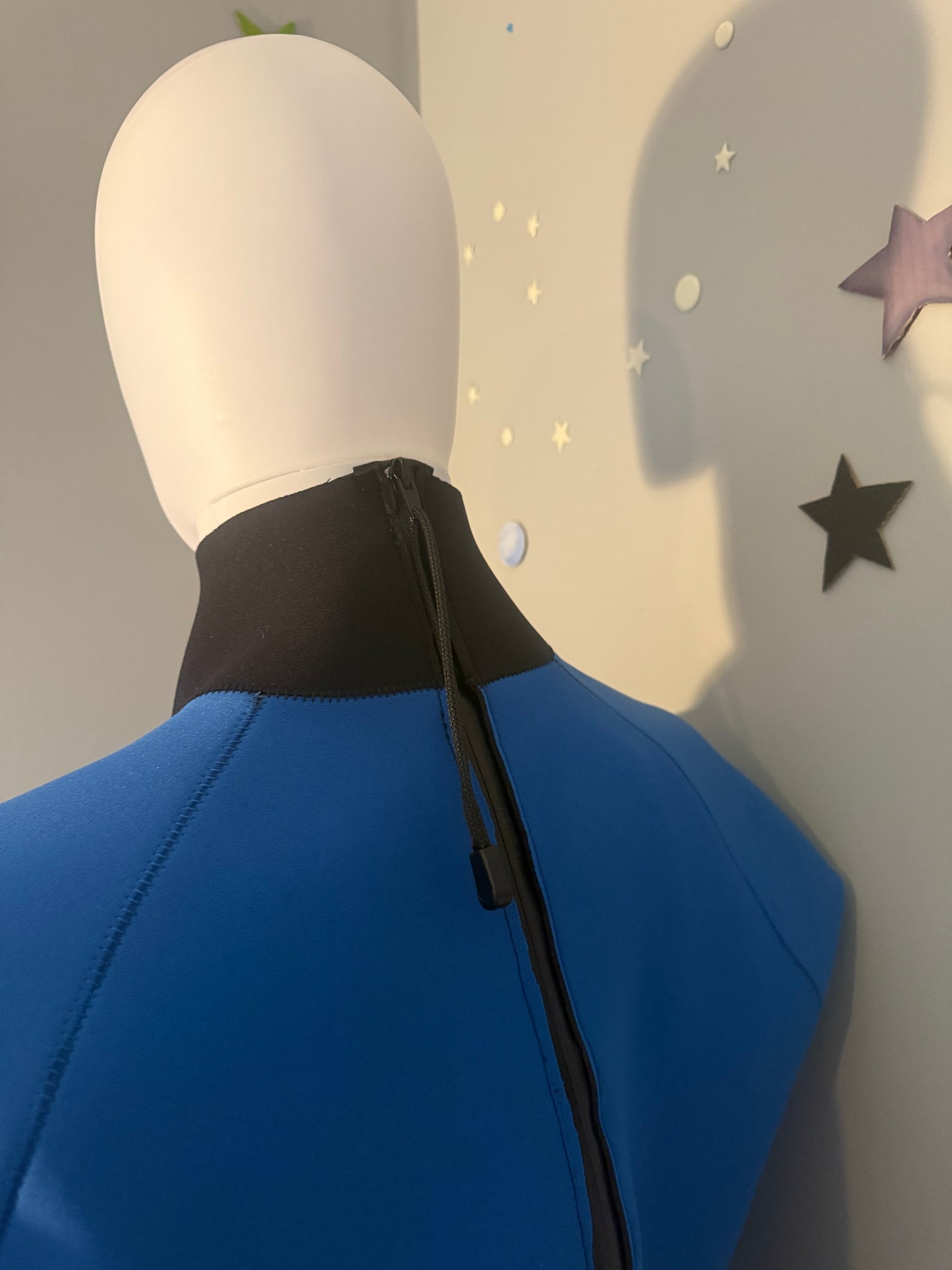 Close-up back view of a blue and black collared Seaspray tuilik displayed, with a black zipper running down the center. 