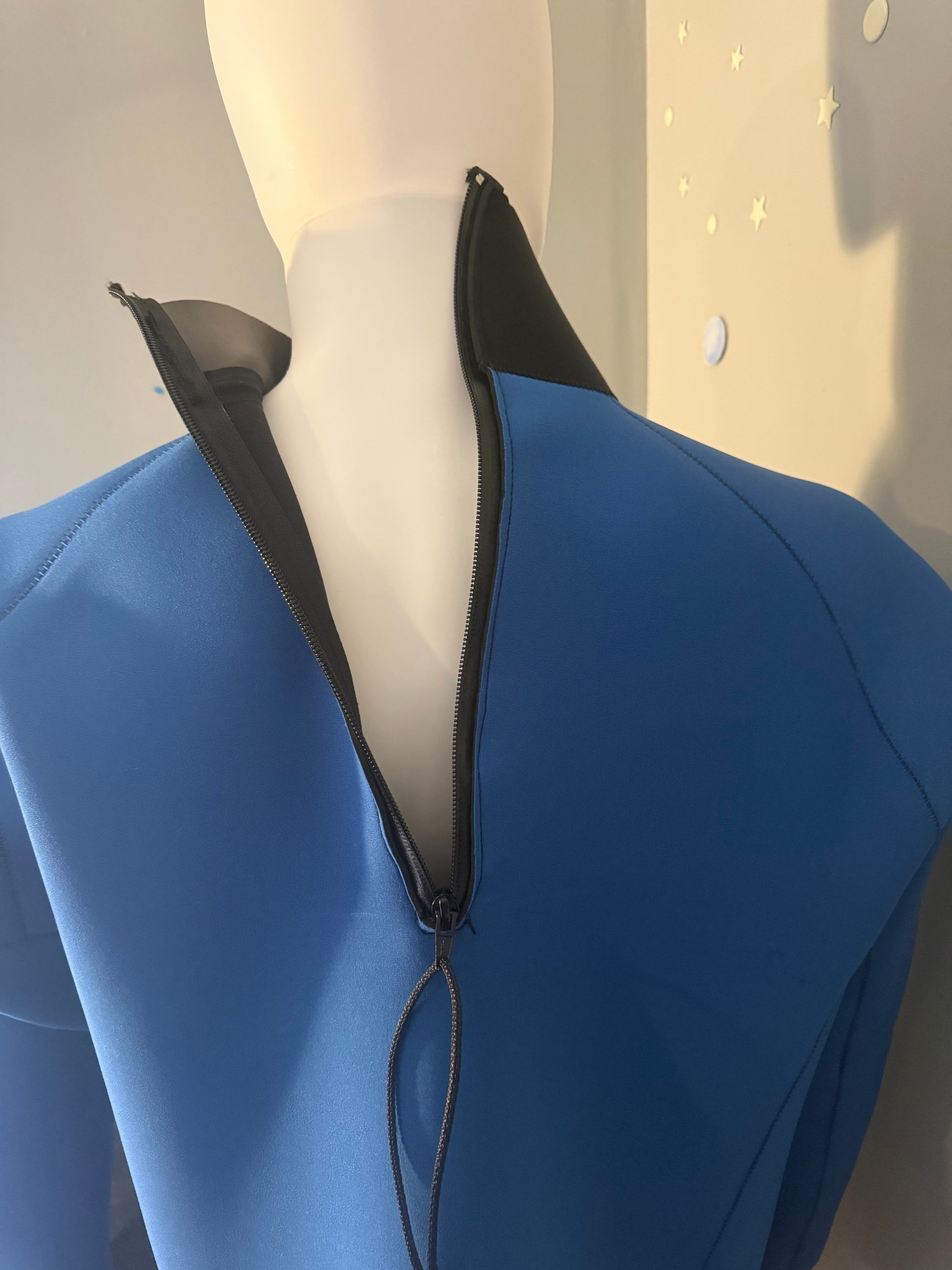Close-up back view of a blue and black collared Seaspray tuilik with a black half zipper running down the center back.